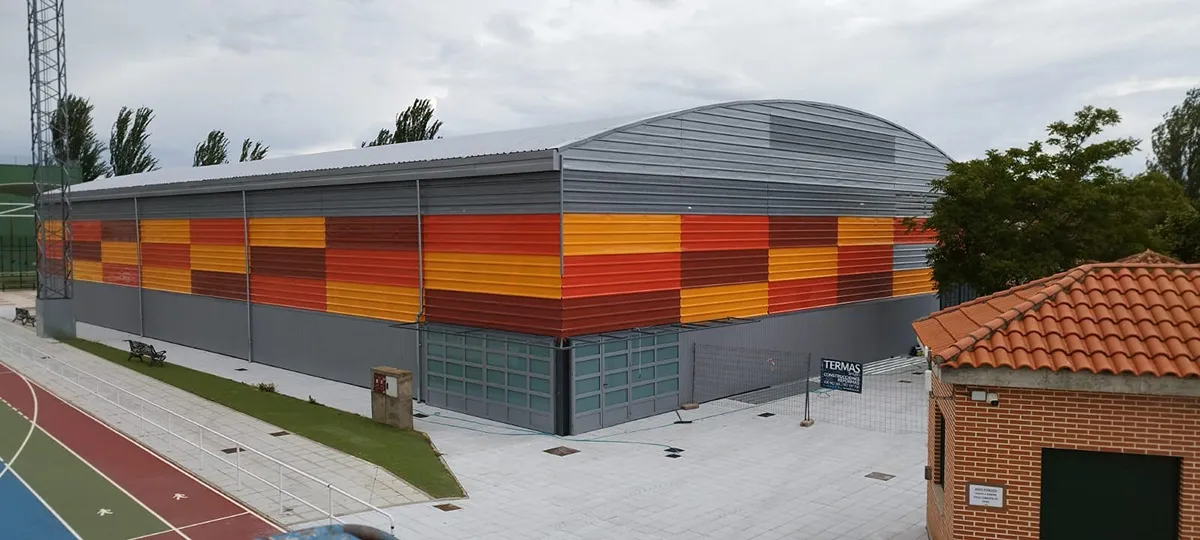 Fachada de polideportivo con chapa trapezoidal en colores rojo, naranja y amarillo, instalación moderna y resistente